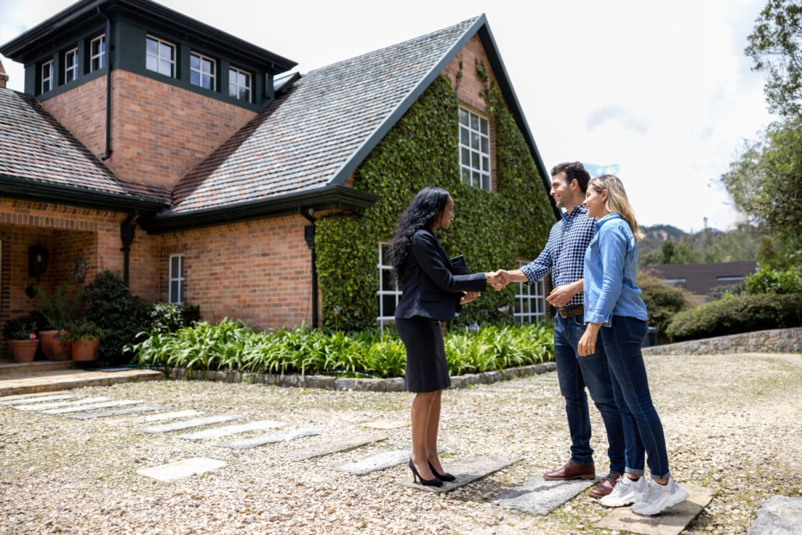 Realtor shaking hands with couple outside home.