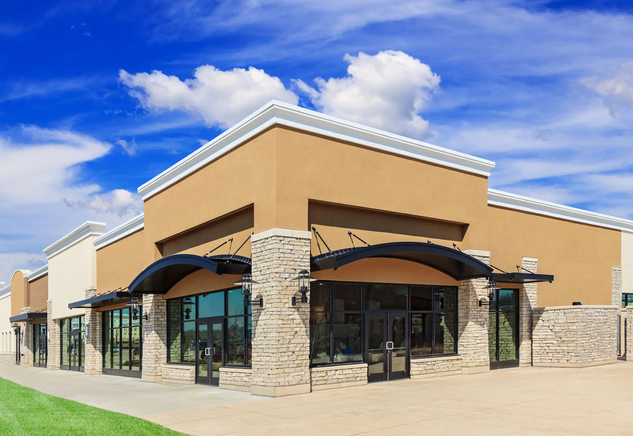 Modern commercial building with stone pillars and large glass windows under a blue sky.